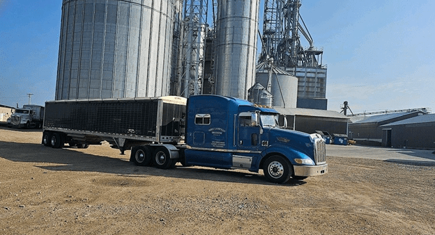 A blue truck parked in front of some silos.
